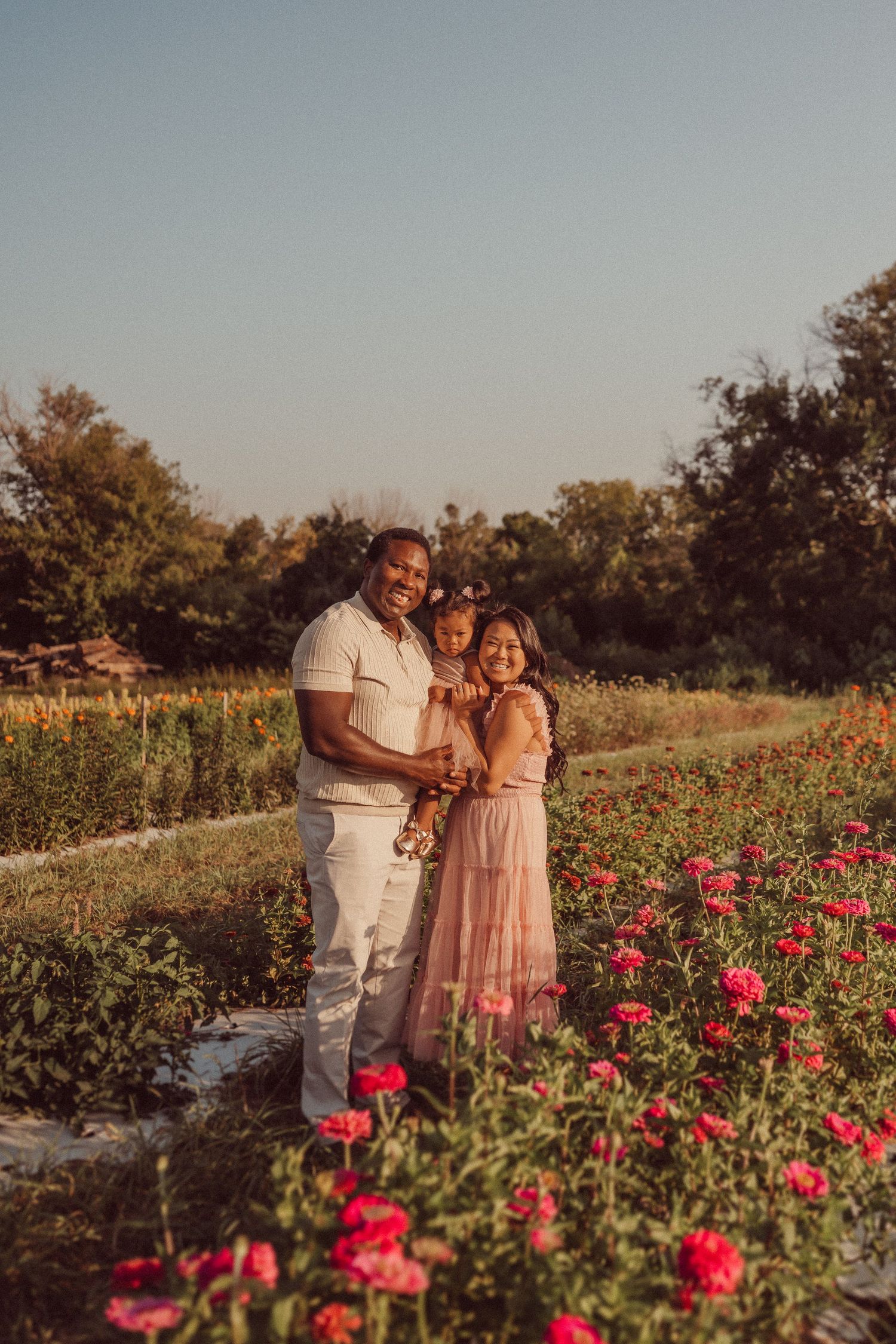 Family portrait in a garden with beautiful red flowers during sunset.