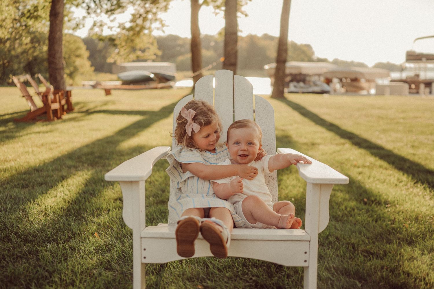 White Adirondack chair in sunlit grass with golden evening light filtering through trees.
