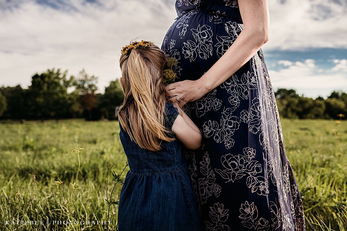 Sweet maternal moment captured in flowering field under dramatic summer sky.
