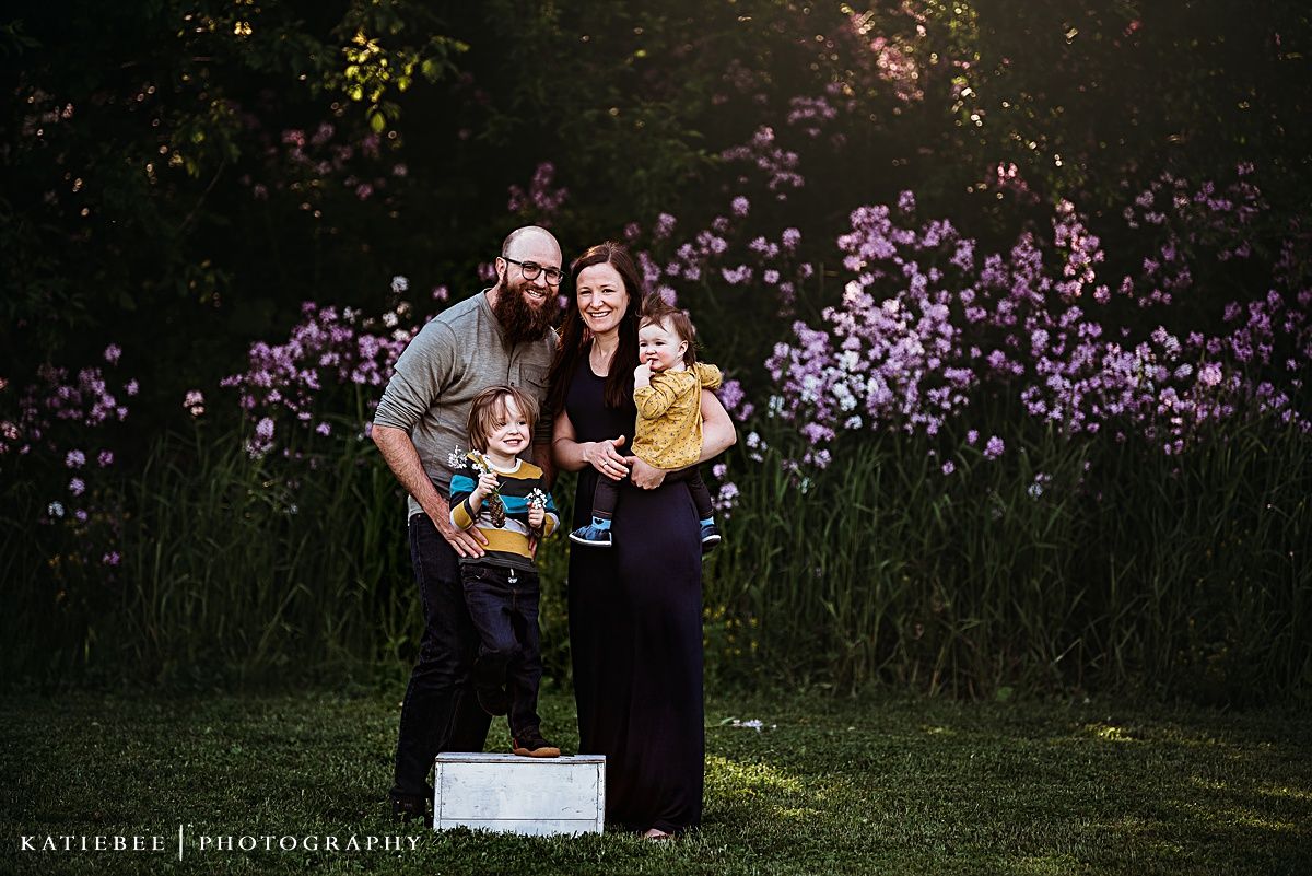 Family standing together against beautiful purple flower garden at sunset.