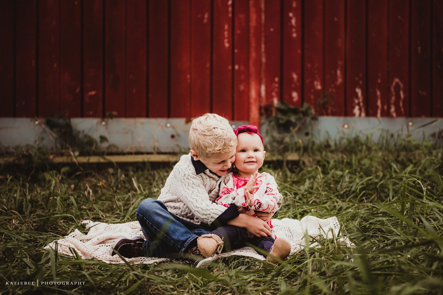 A sweet moment of bonding captured outdoors against a rustic red barn backdrop.
