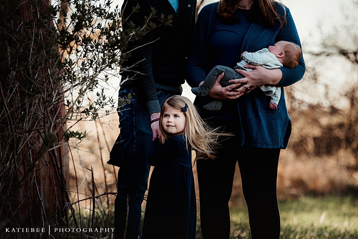 Outdoor family portrait with parents and children dressed in blue and black against autumn trees.