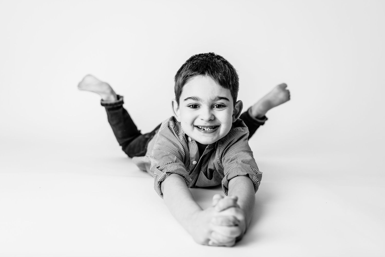 Child lying on stomach with raised arms in playful black and white portrait.