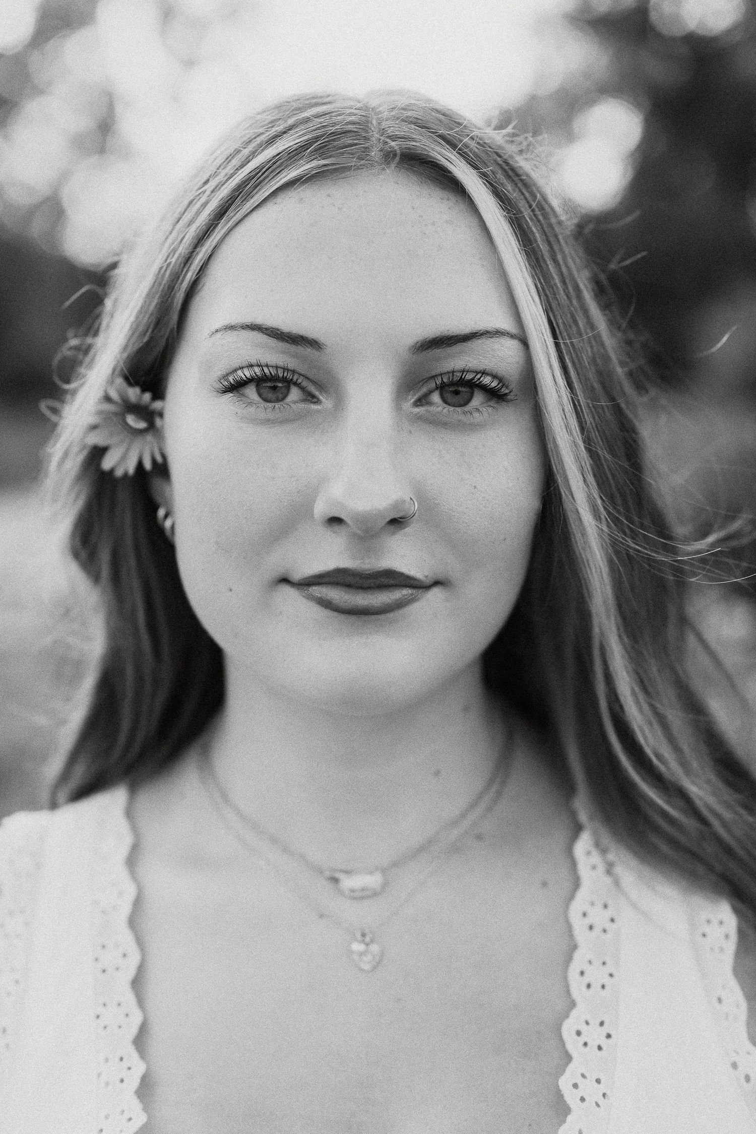 Black and white portrait of a young woman with long hair and a flower tucked behind her ear.