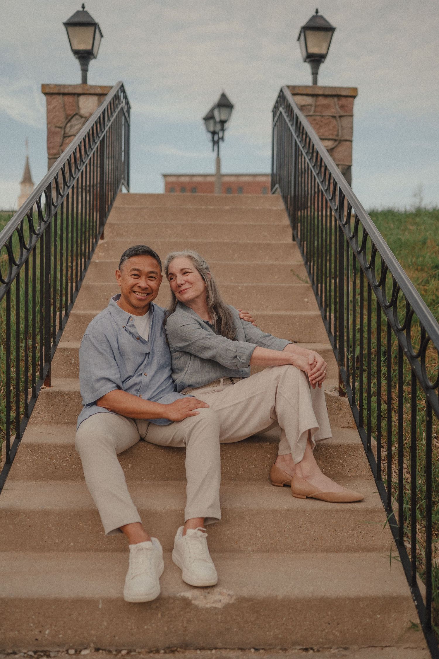 Happy interracial couple sitting together on outdoor stone steps near a bridge.