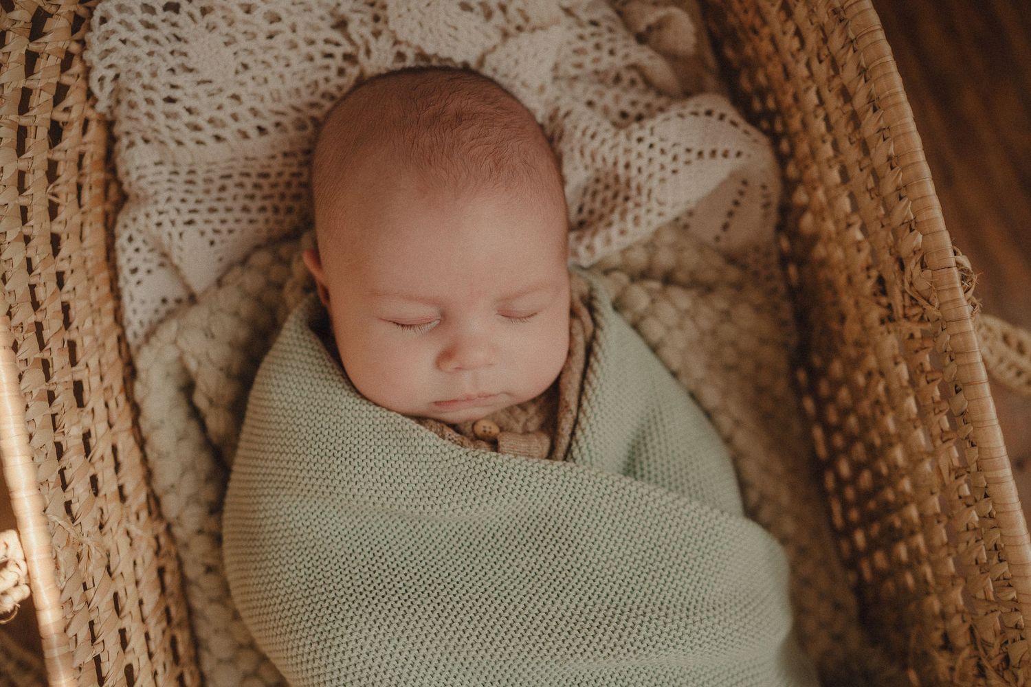 Newborn baby sleeping peacefully in woven basket with warm toned lighting.