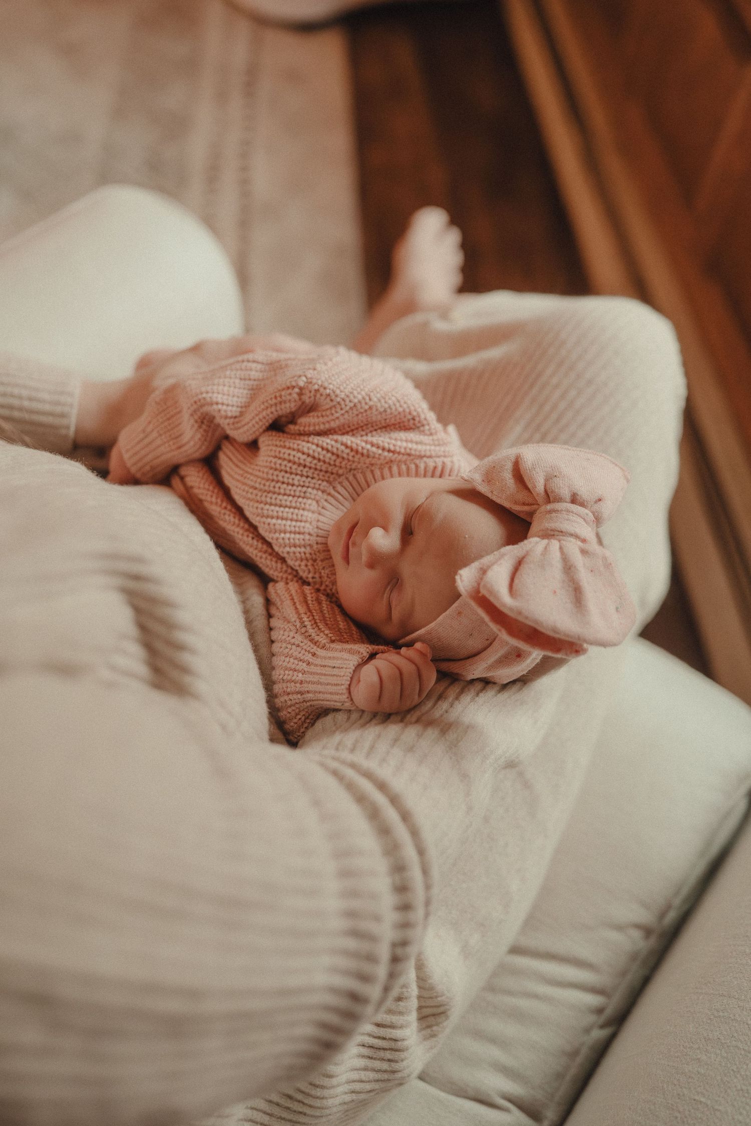 A sleeping baby wrapped in a cozy pink knit sweater rests peacefully on white bedding.