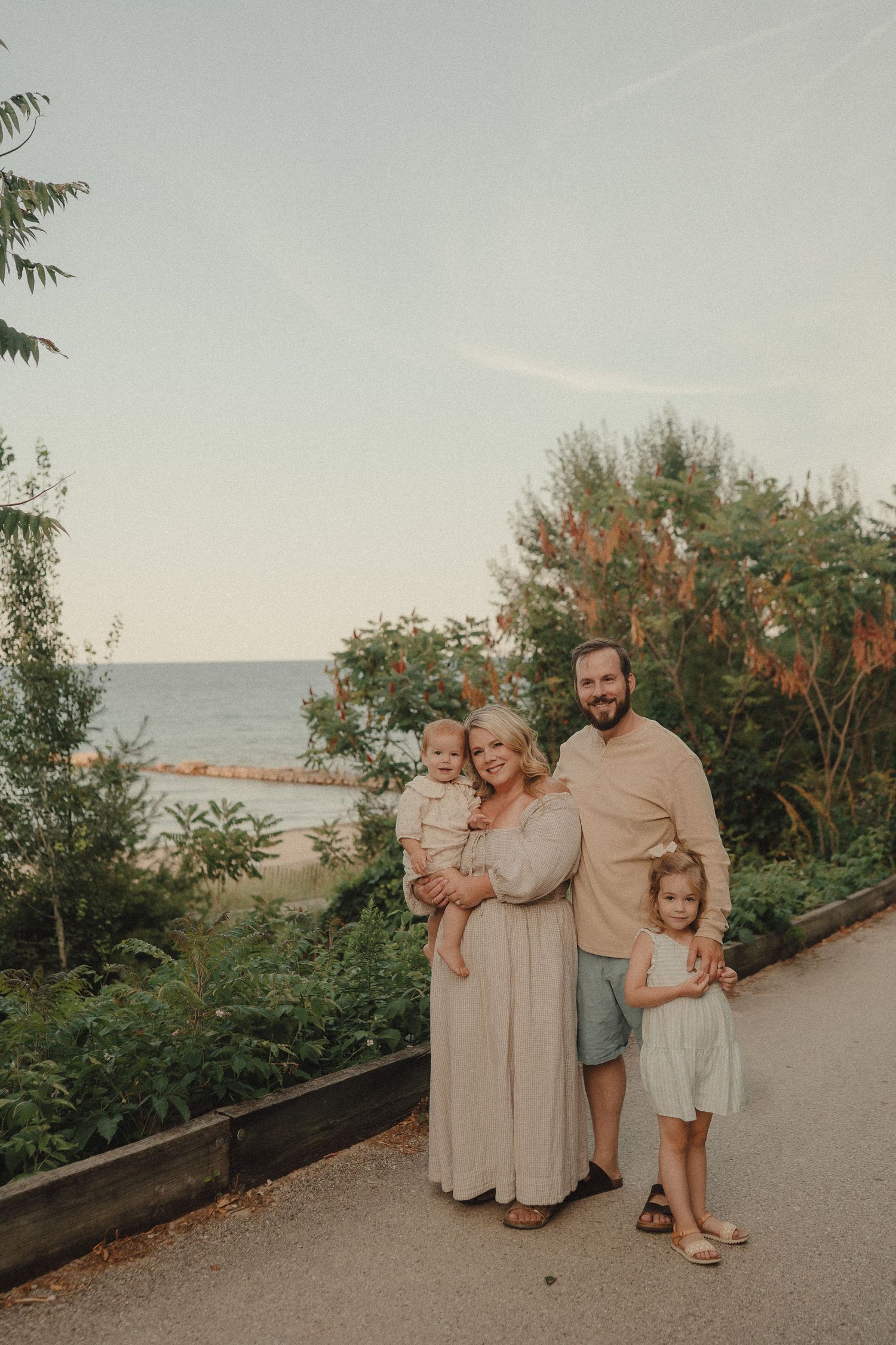 Family of four posing on scenic coastal path surrounded by lush greenery with ocean view behind them.
