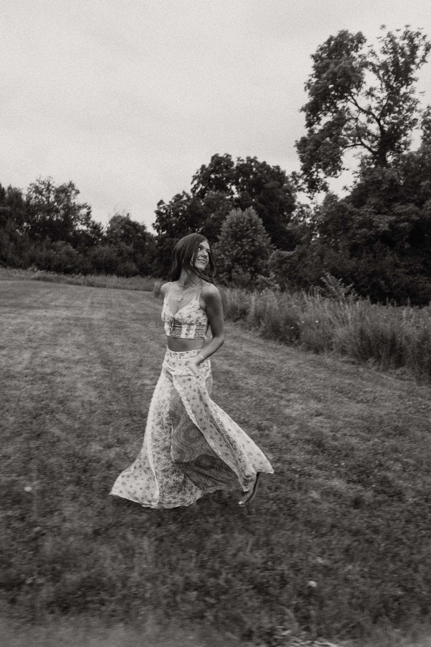 Black and white photo of a woman in a floral two-piece outfit walking through a grassy field.