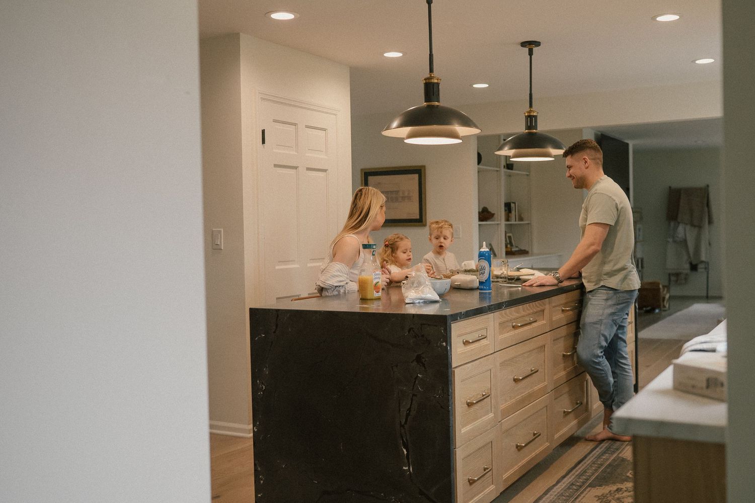 Family gathered around a dark marble kitchen island with pendant lights in a modern home.