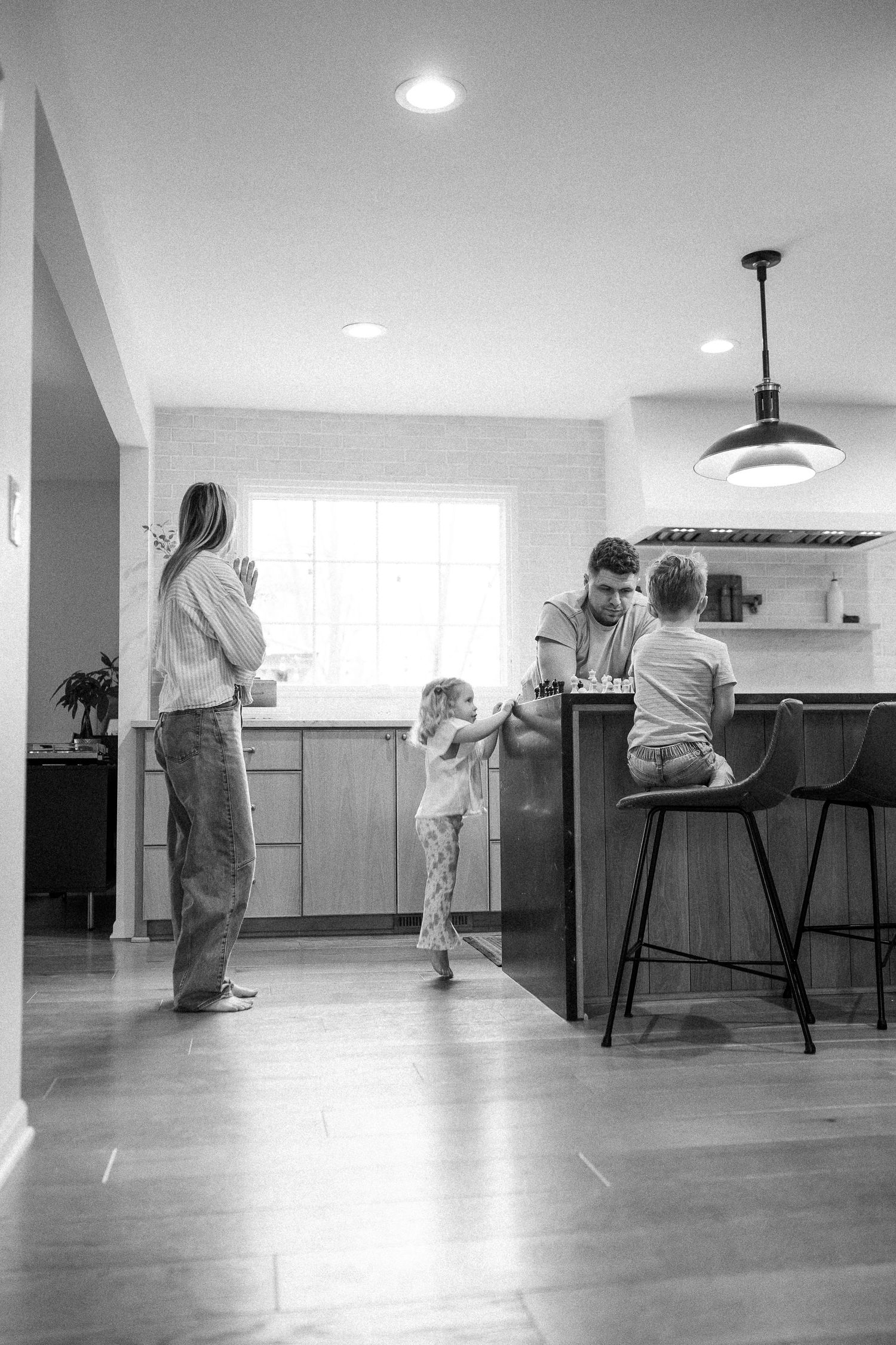 Black and white wide-angle photo of a family in a modern kitchen, with a child dancing in the center.