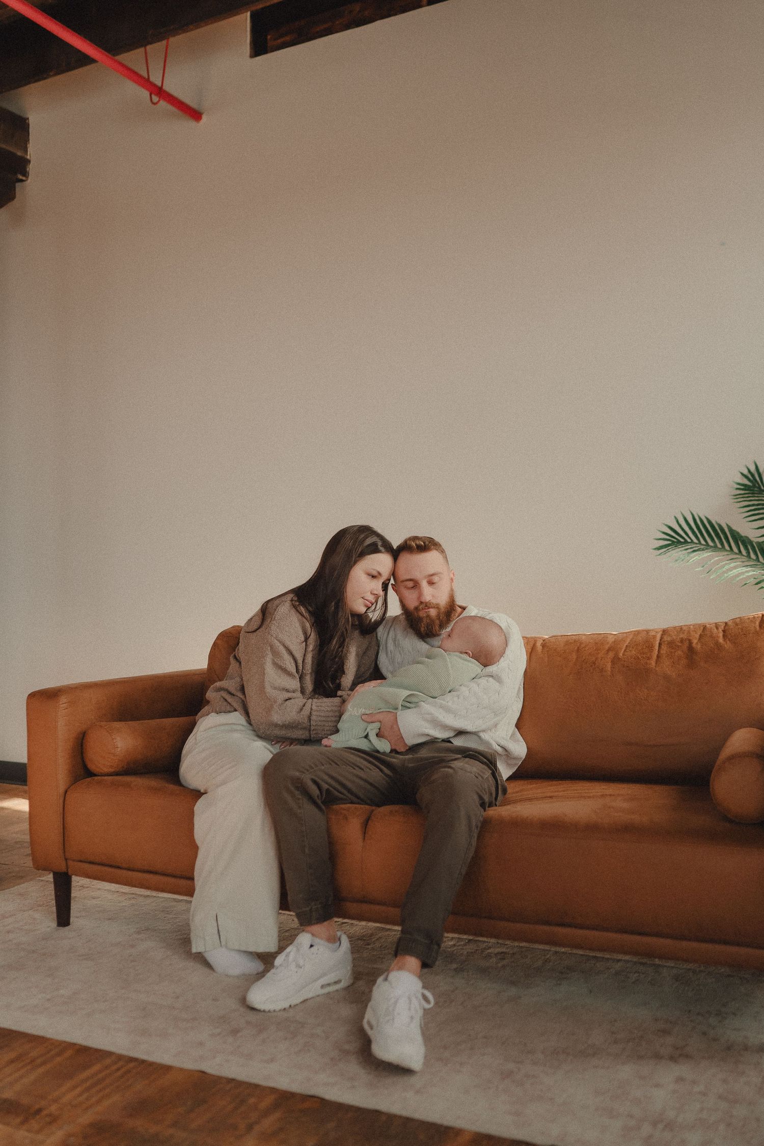 Couple sharing intimate moments on a brown leather couch in a modern industrial space with concrete floors.