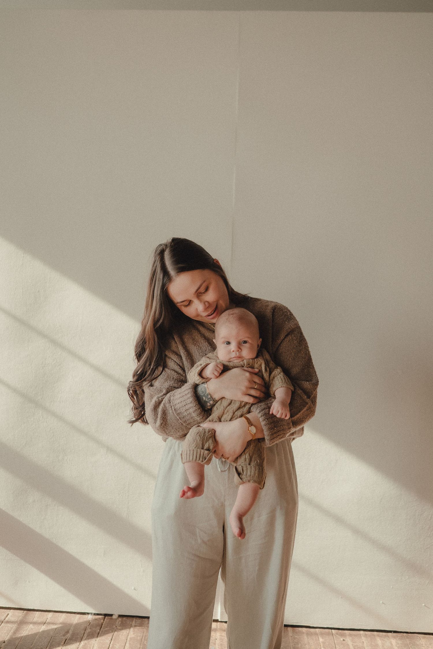 Lifestyle photography of parent and infant in soft natural light wearing neutral colored clothing.