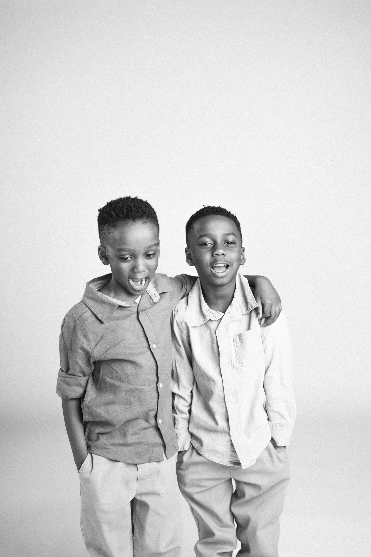 Two children in casual attire share a playful moment against a white background.