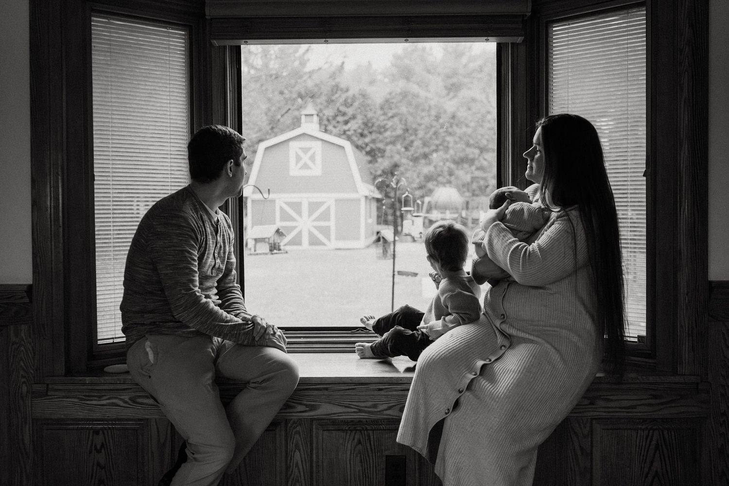 A silhouetted scene of a family gathering by large windows with natural backlighting.