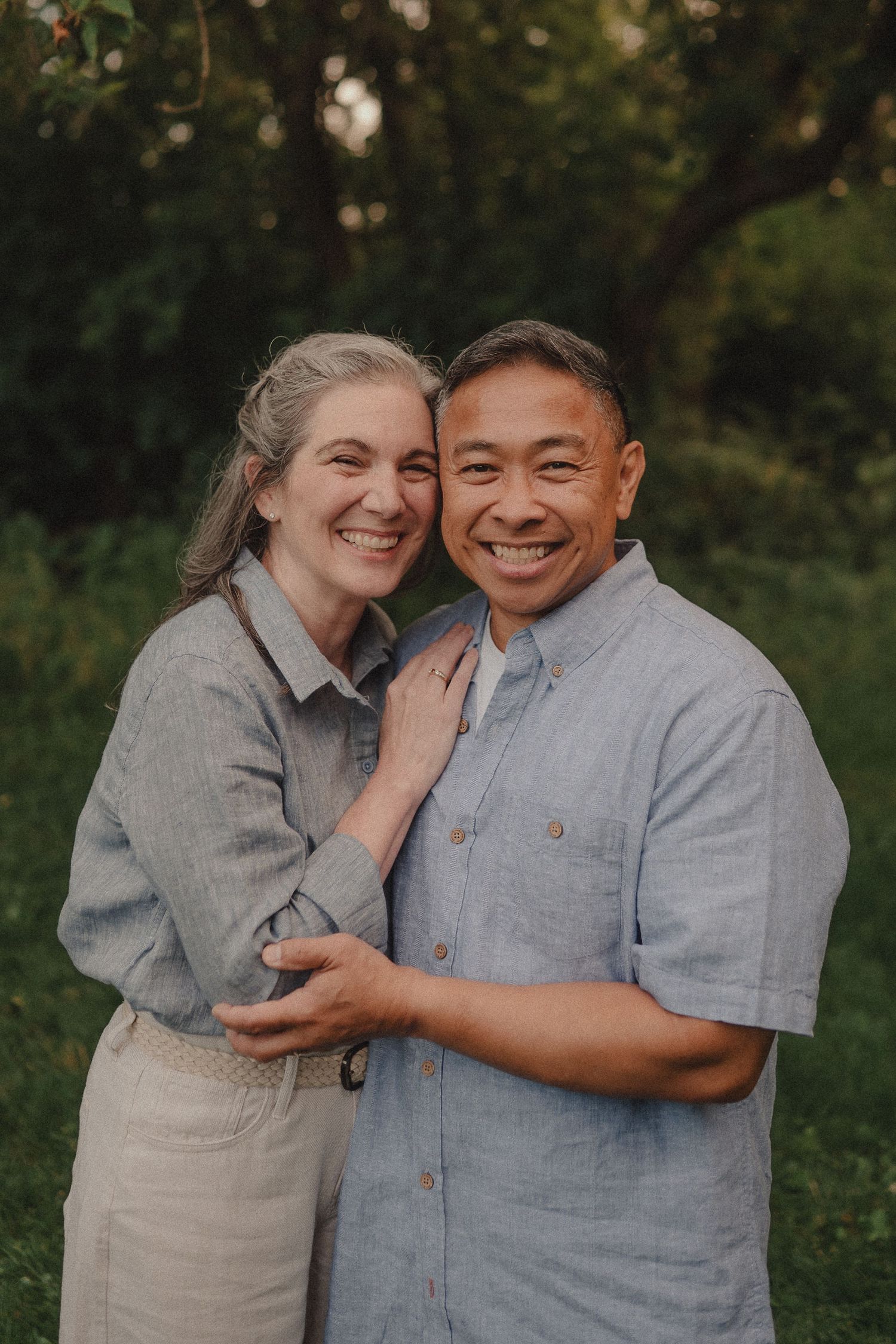 Smiling interracial couple embracing outdoors in a lush green garden setting.