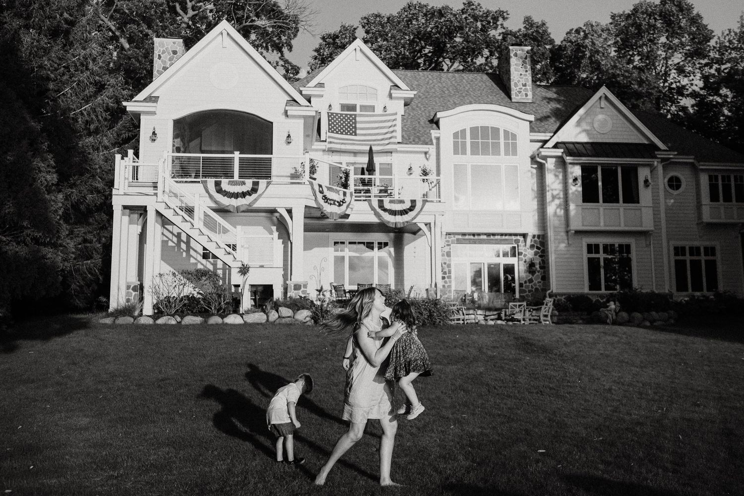 Black and white photo of children playing in yard of large elegant two-story home.
