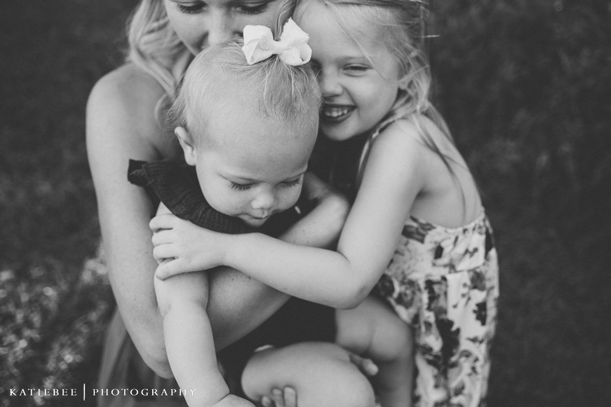 Black and white candid photography of joyful family embracing outdoors in natural light.