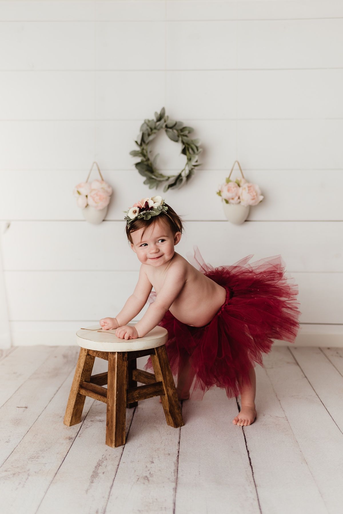 Rustic photo setup with wooden stool, burgundy tutu, and wall decorations.
