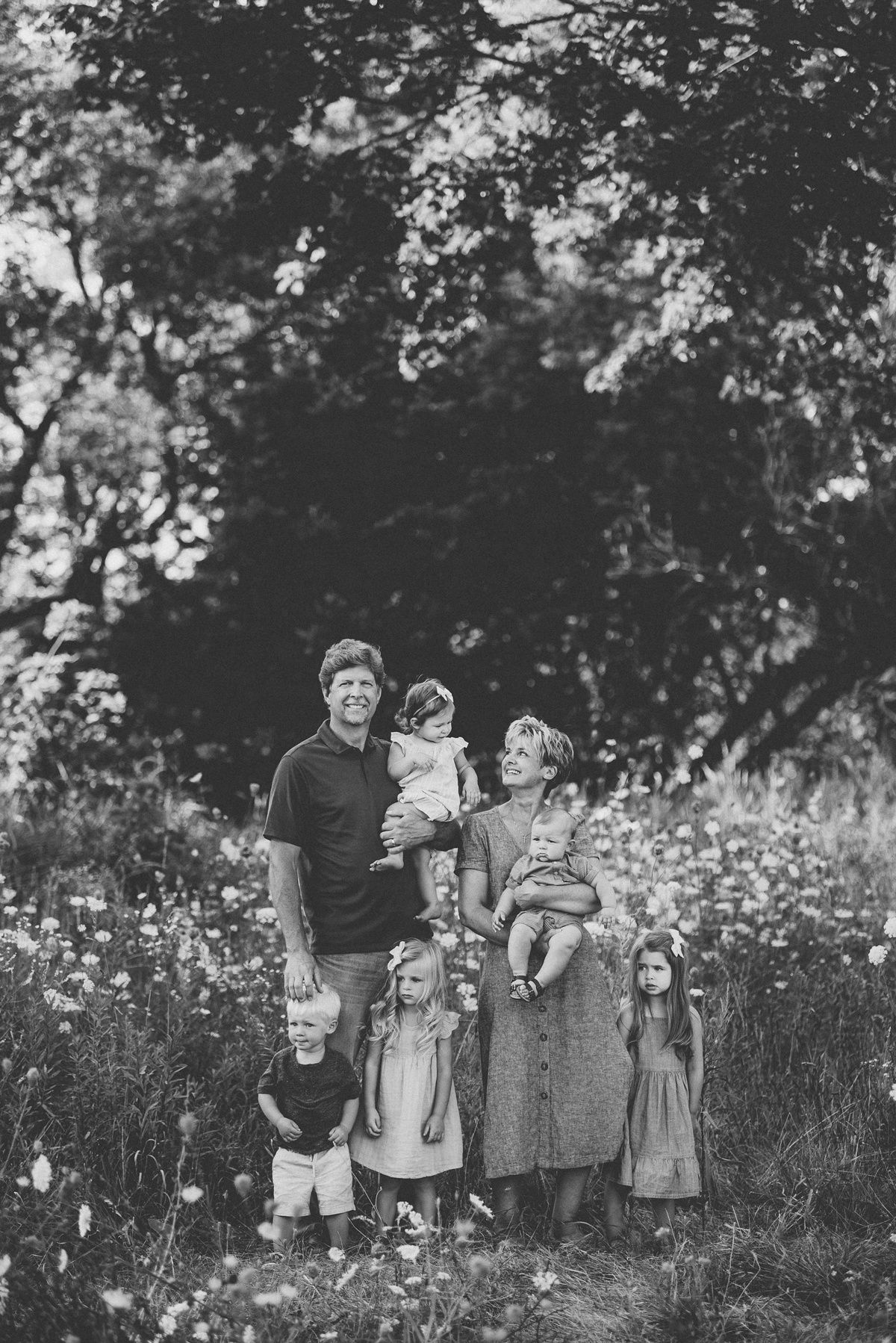 Black and white family portrait in a wildflower meadow with trees in the background.