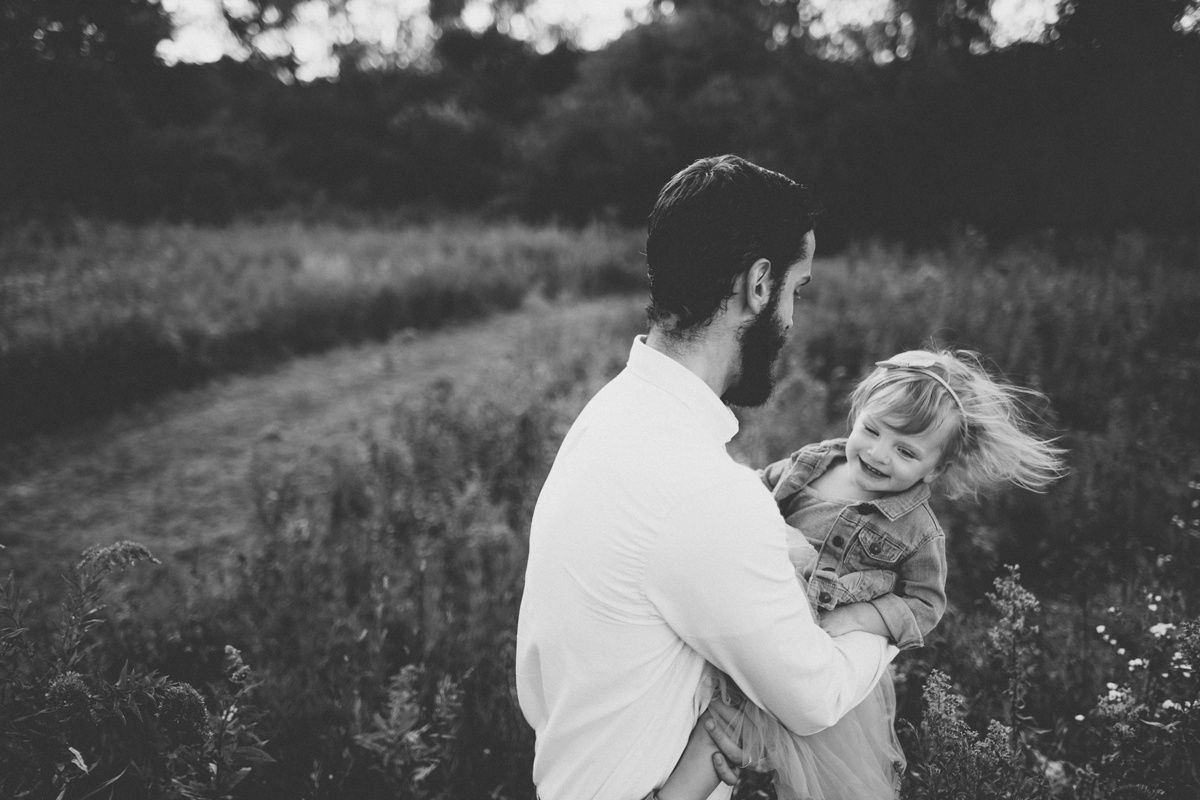 Black and white photo of parent swinging child in a wildflower meadow.