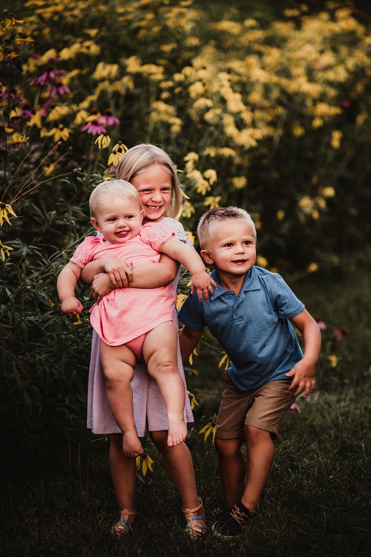 Children playing and laughing together in garden with yellow flowers blooming.