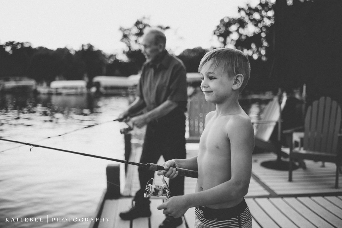 A shirtless young boy and adult fishing together on a wooden dock.