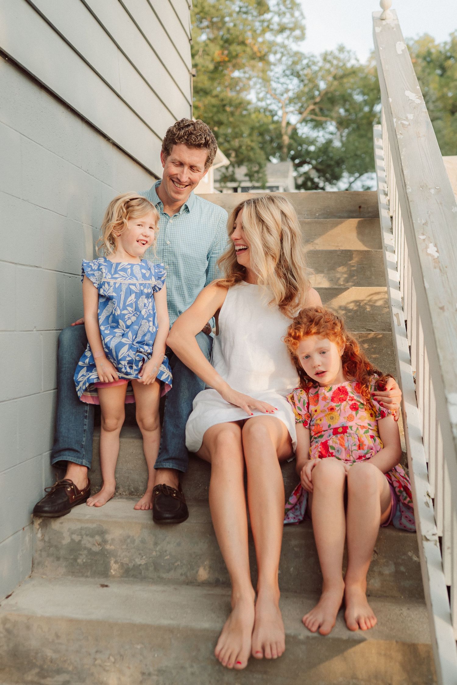 Family sharing laughs while sitting together on concrete steps outdoors.