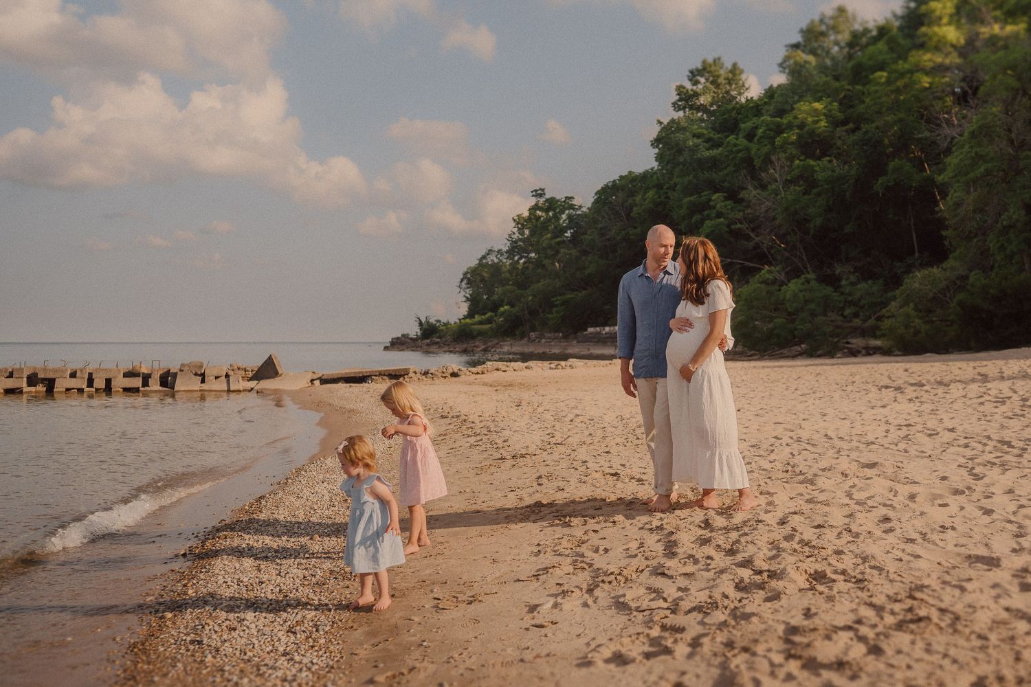 Family enjoying a serene beach walk during golden hour with waves and rocks visible along shoreline.