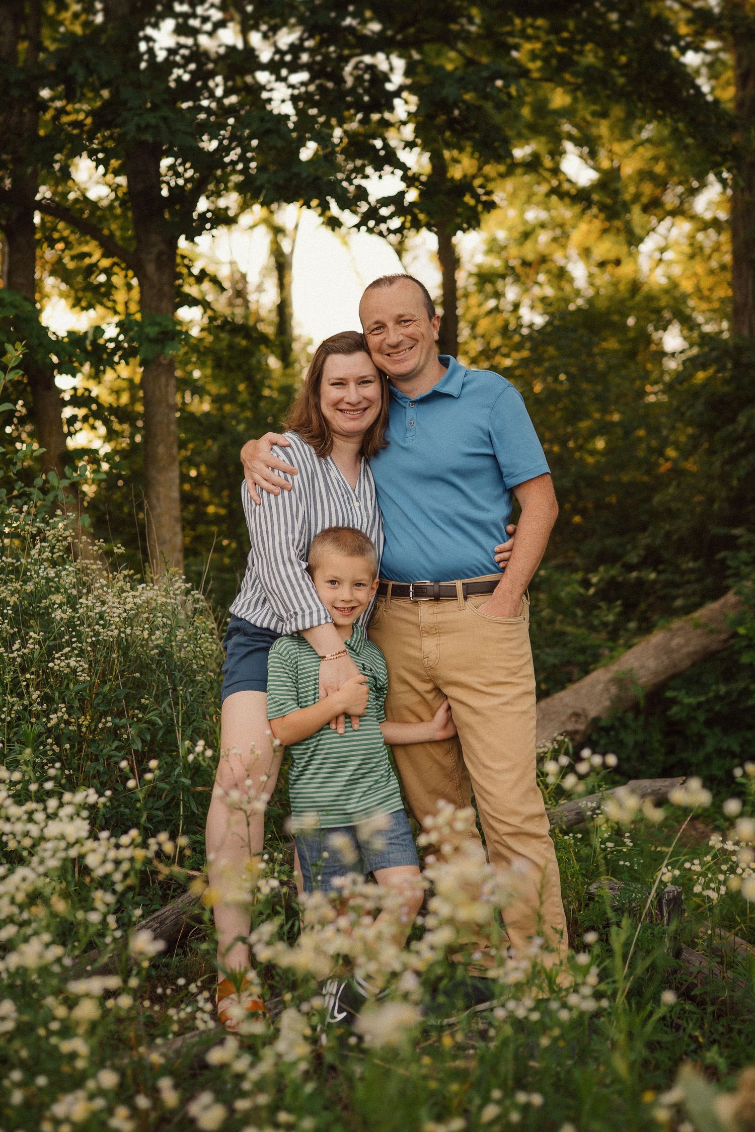 A family poses together outdoors at golden hour surrounded by wildflowers and trees.