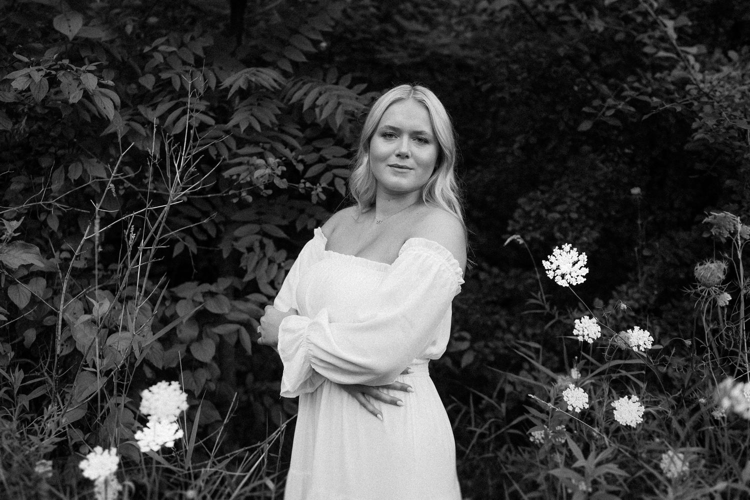 A black and white artistic photo collage shows a person in white clothing among flowers and foliage in a garden setting.