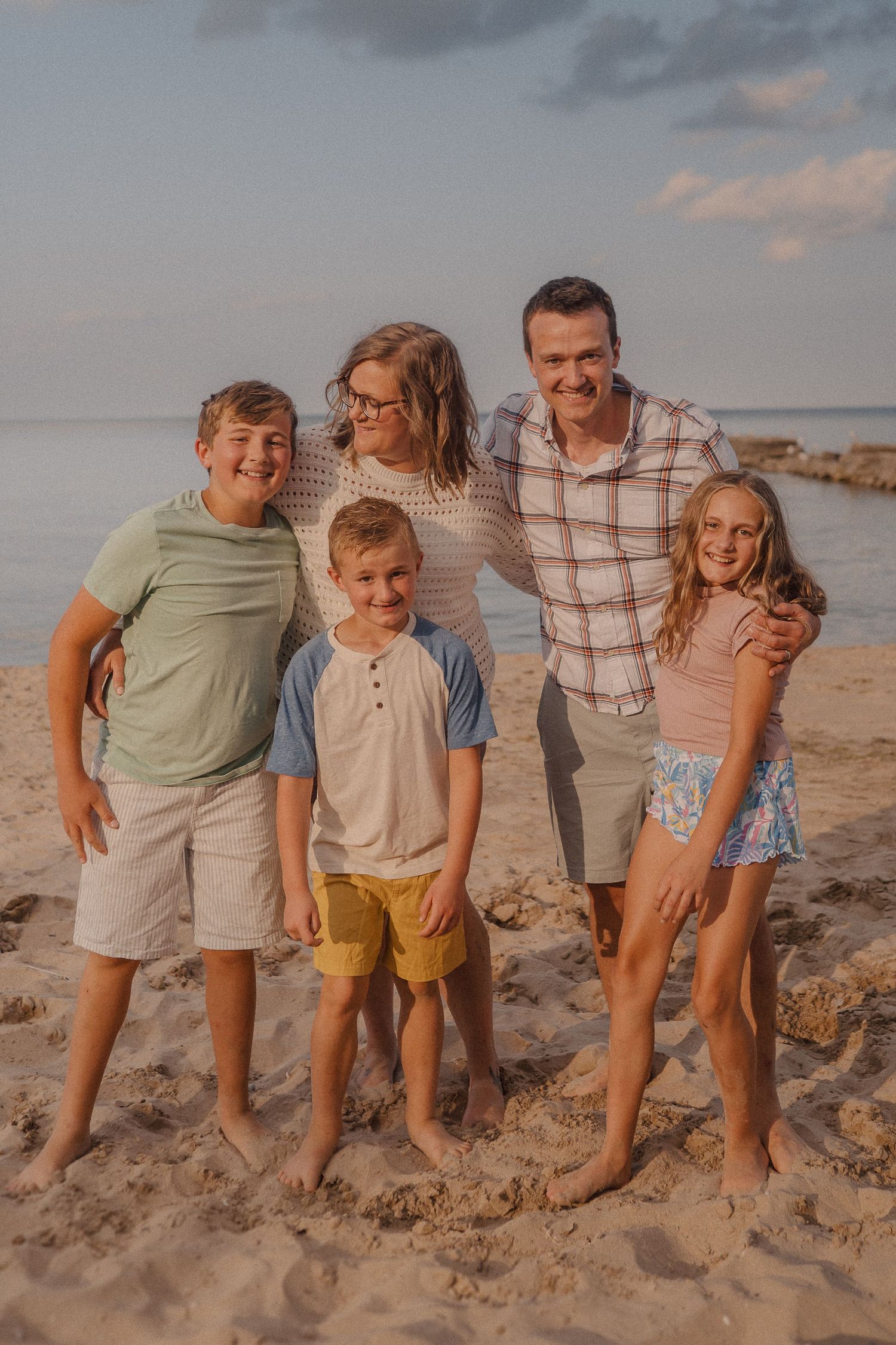 Family group poses together on a rocky beach at sunset.