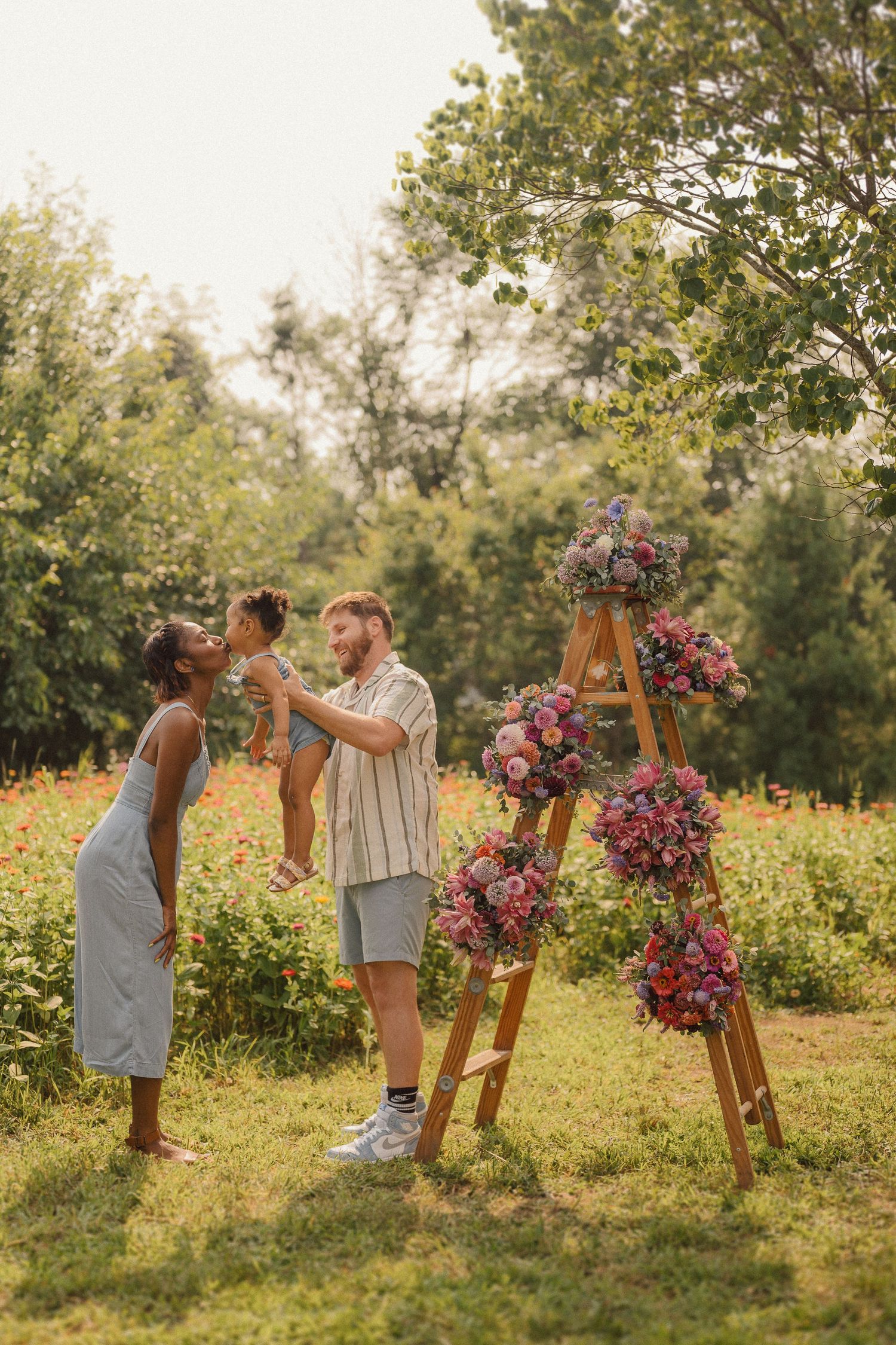 Summer outdoor photoshoot with decorative wooden ladder featuring cascading pink and purple flower arrangements.