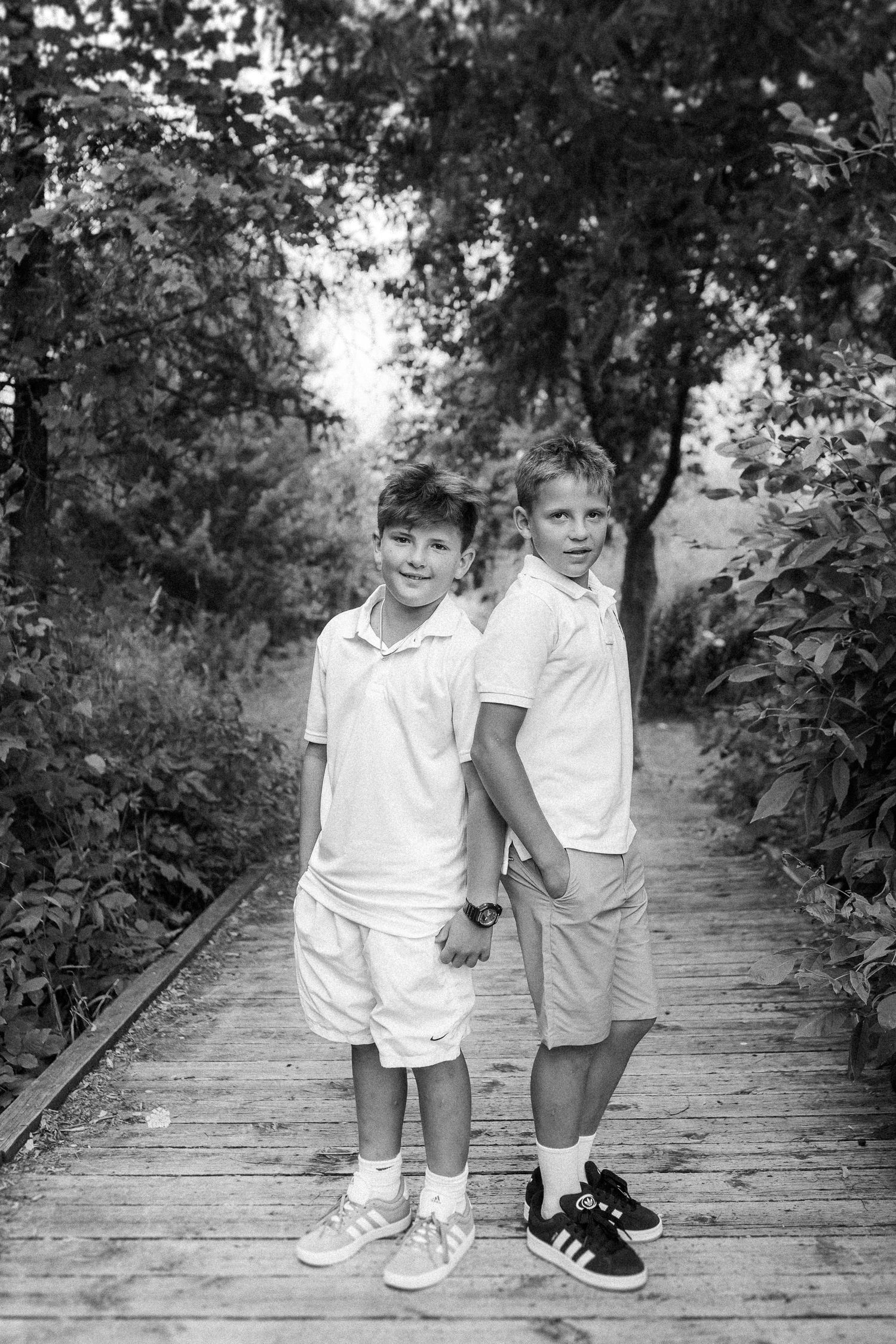 Two young children in white outfits walking together on a wooden boardwalk.