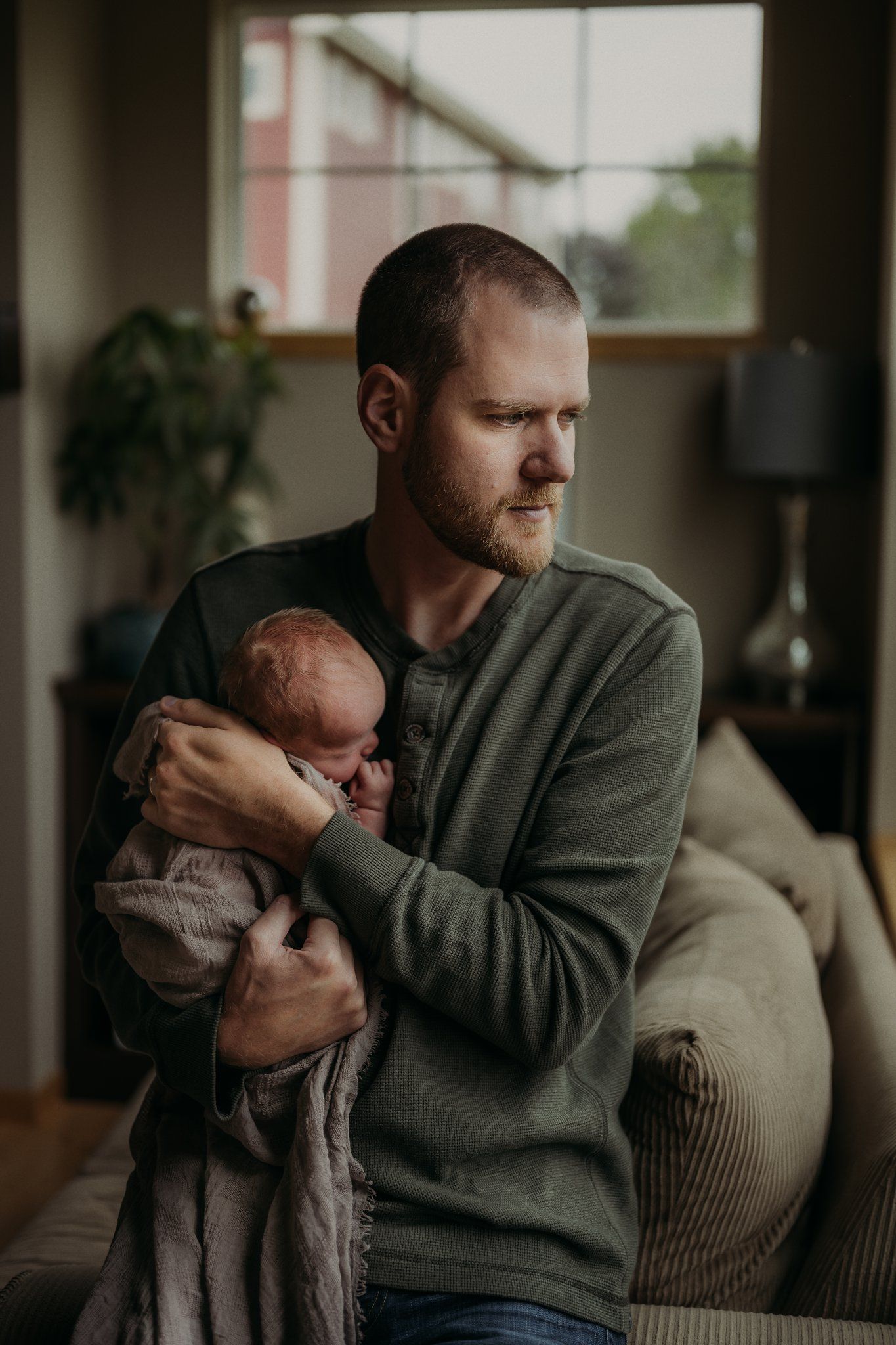 Parent in gray sweater holding sleeping infant in cozy living room.