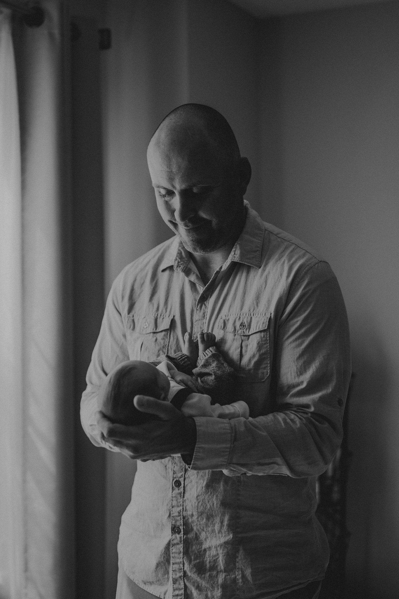 Parent in light colored shirt tenderly holds sleeping newborn in moody lighting.