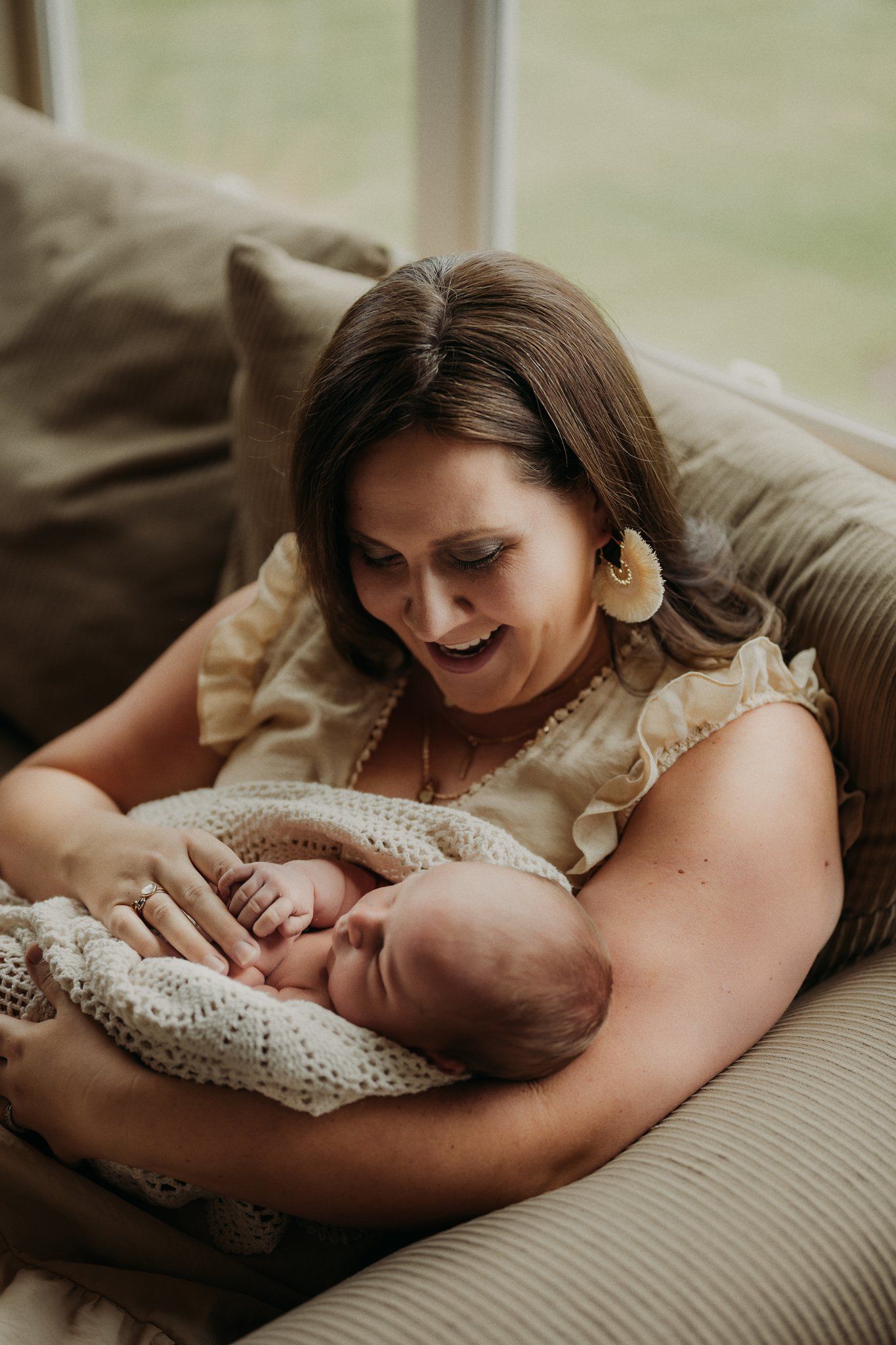 Tender moment captured of parent and newborn resting together on gray couch.