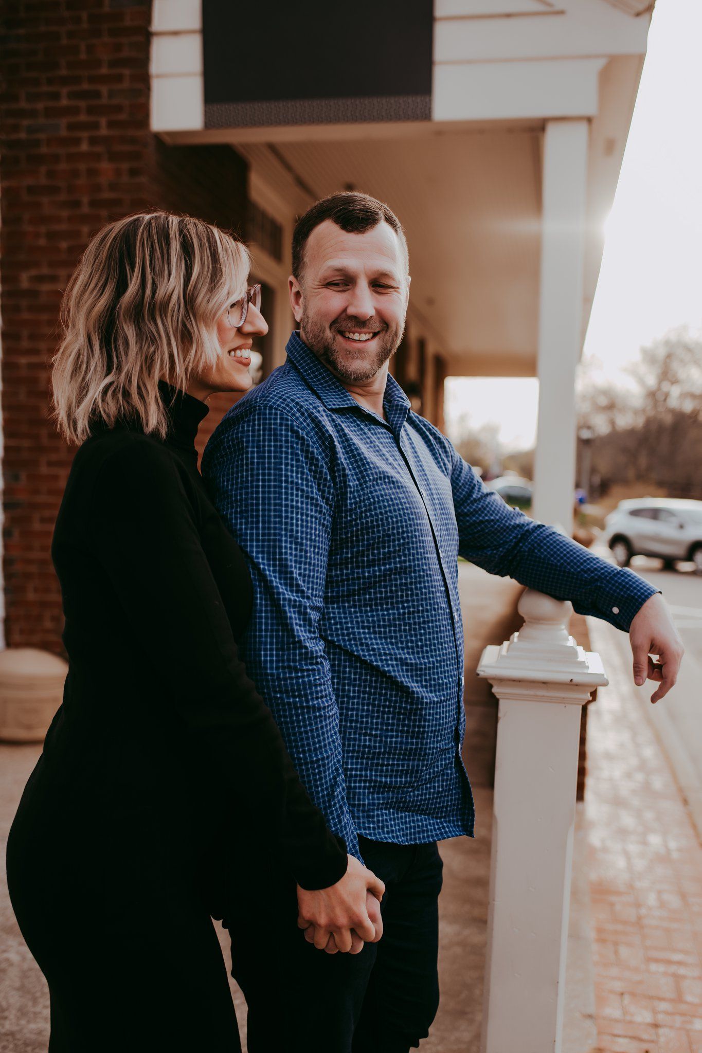 A happy couple shares a candid moment while standing against a brick wall.