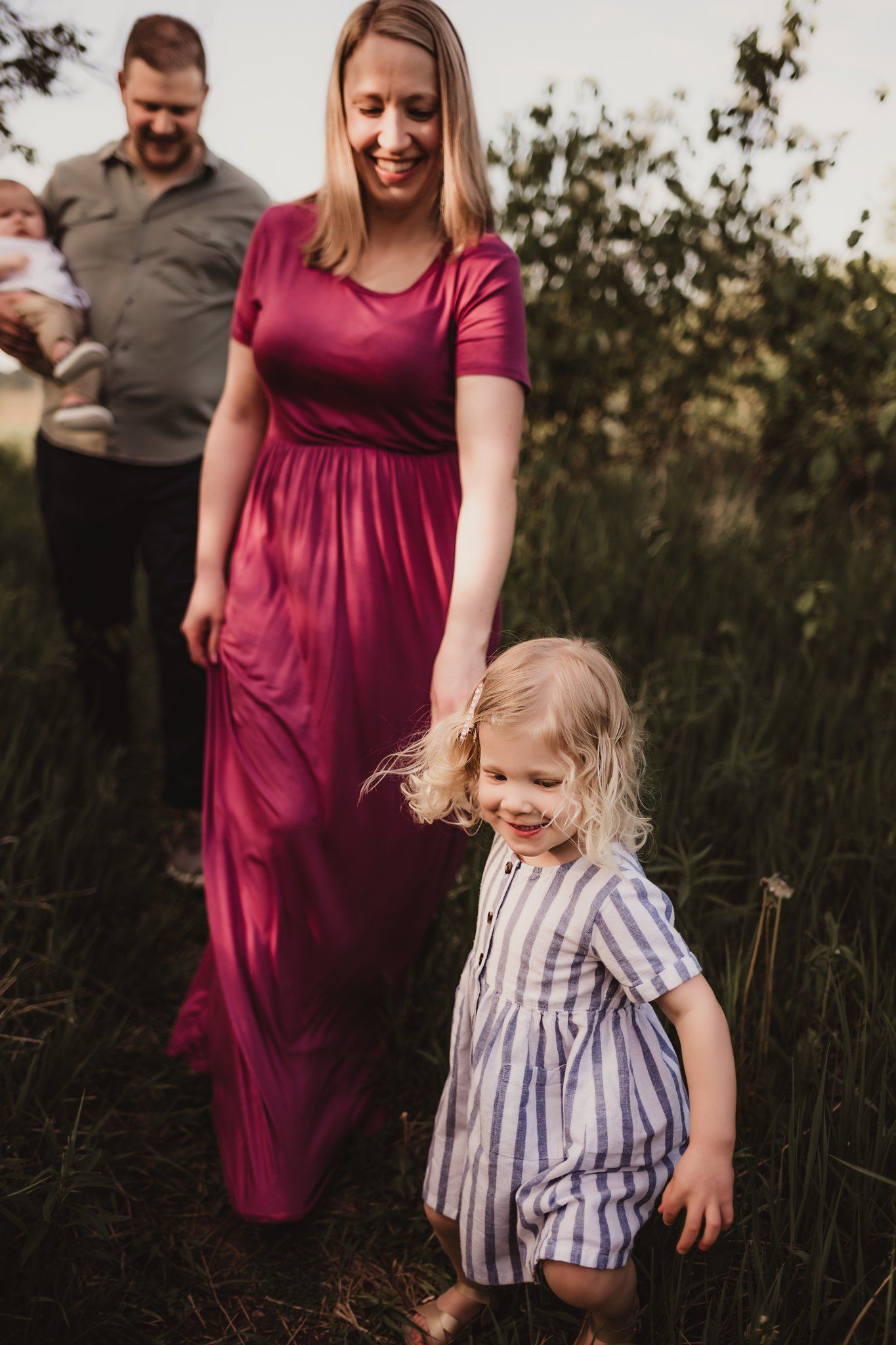 Family walking through tall grass wearing burgundy and neutral tones during sunset session.