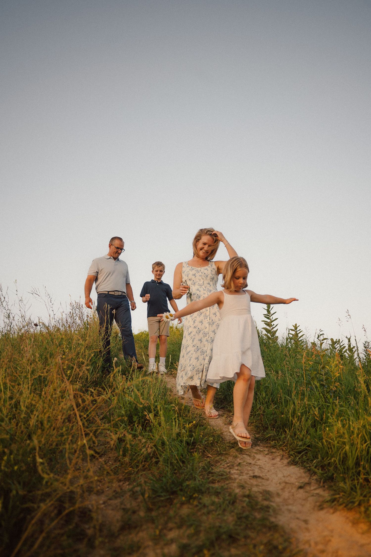 A group walks along a winding dirt path through tall grass at sunset.