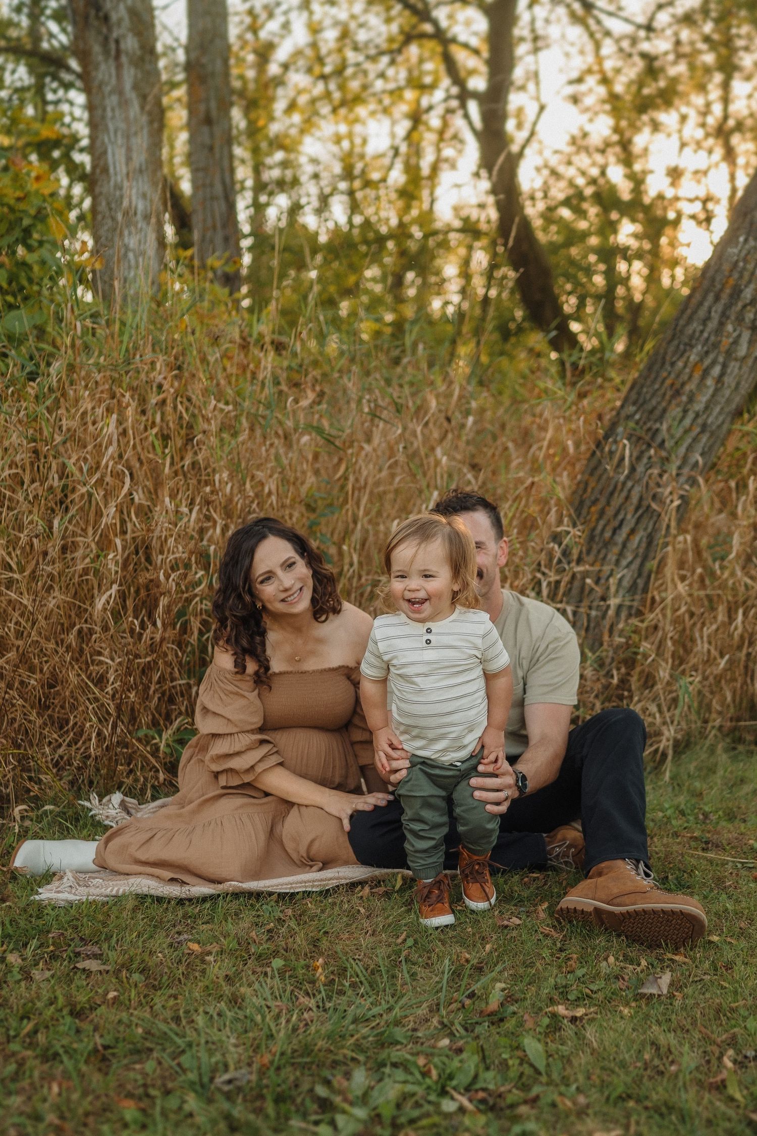 A family sits together on a blanket among tall autumn grasses during golden hour.