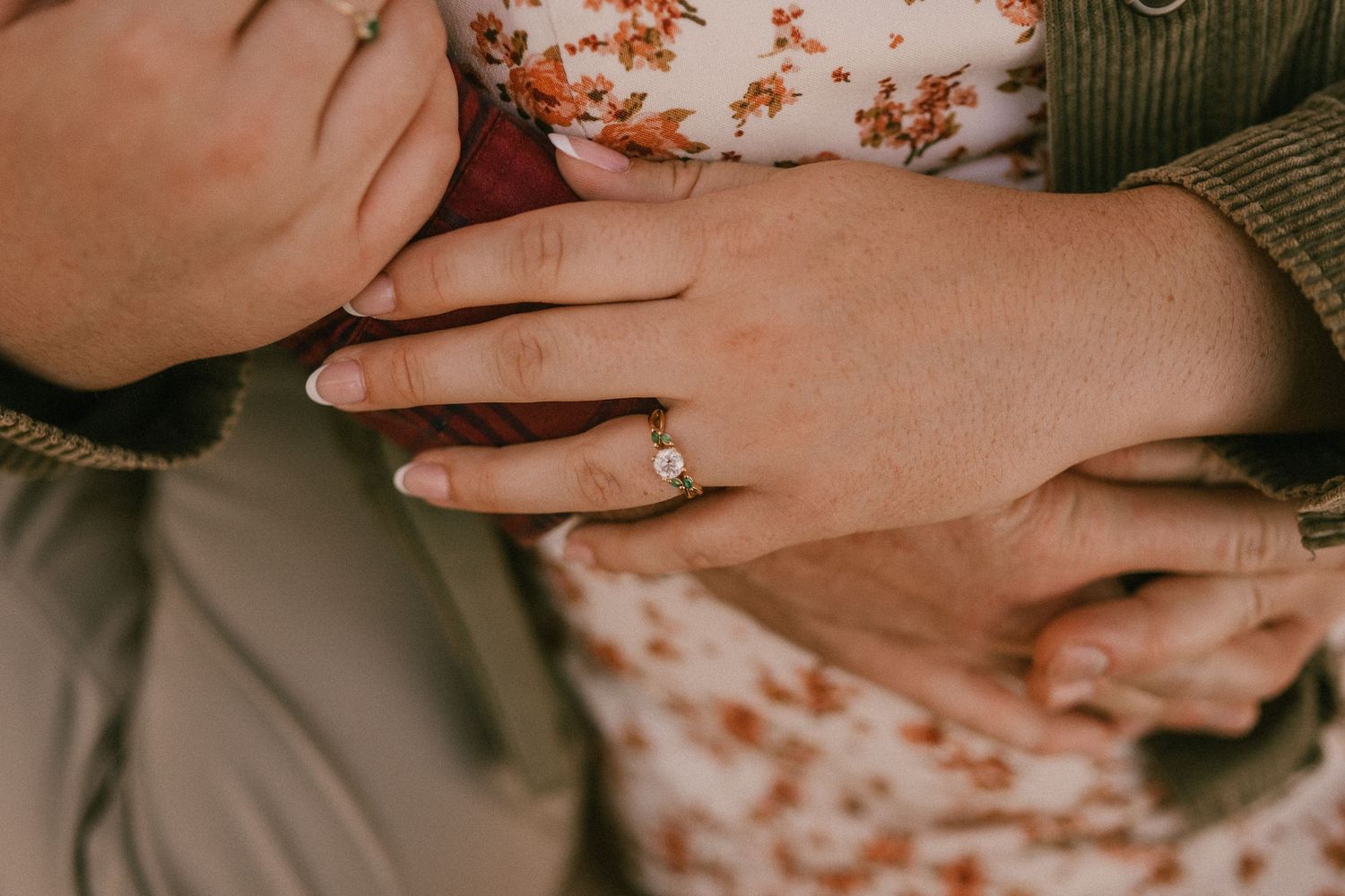 Close up detail of engagement ring on hand with floral dress and sweater in background.