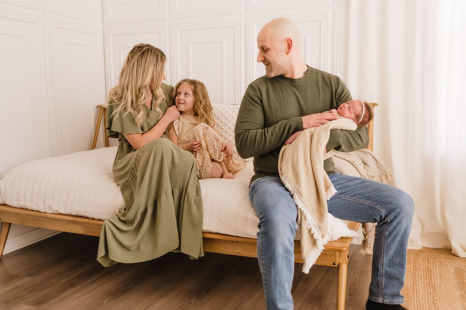 A family wearing olive green shirts sits together on a beige couch in a bright minimalist room.
