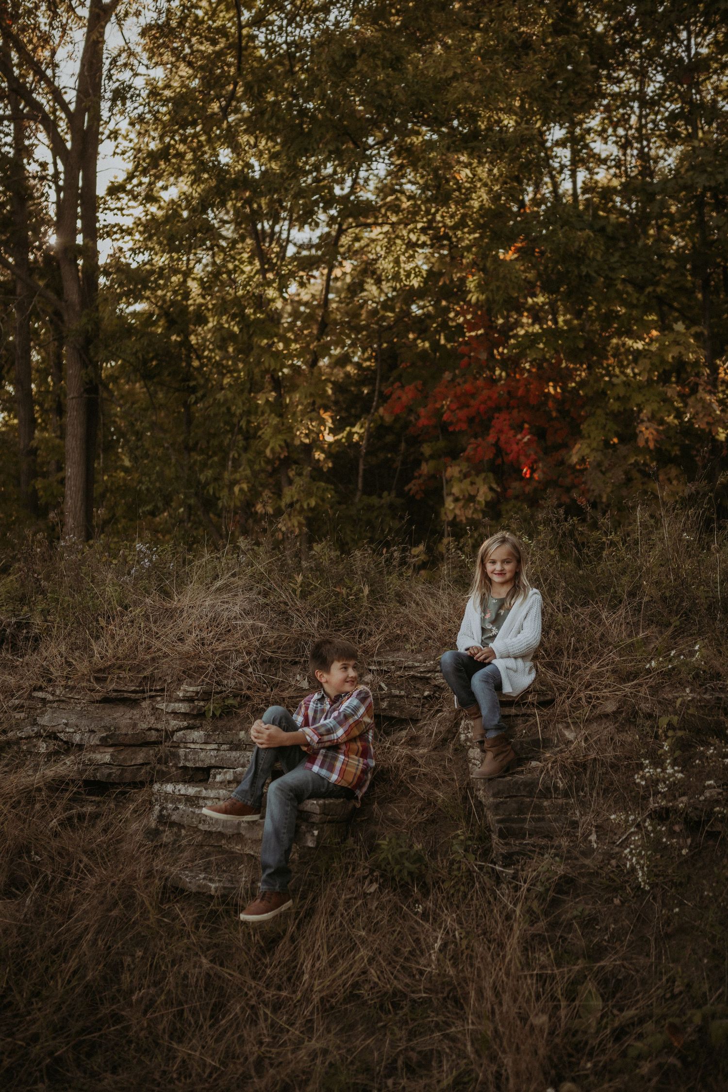 Two people relaxing on natural stone steps in an autumn forest setting.