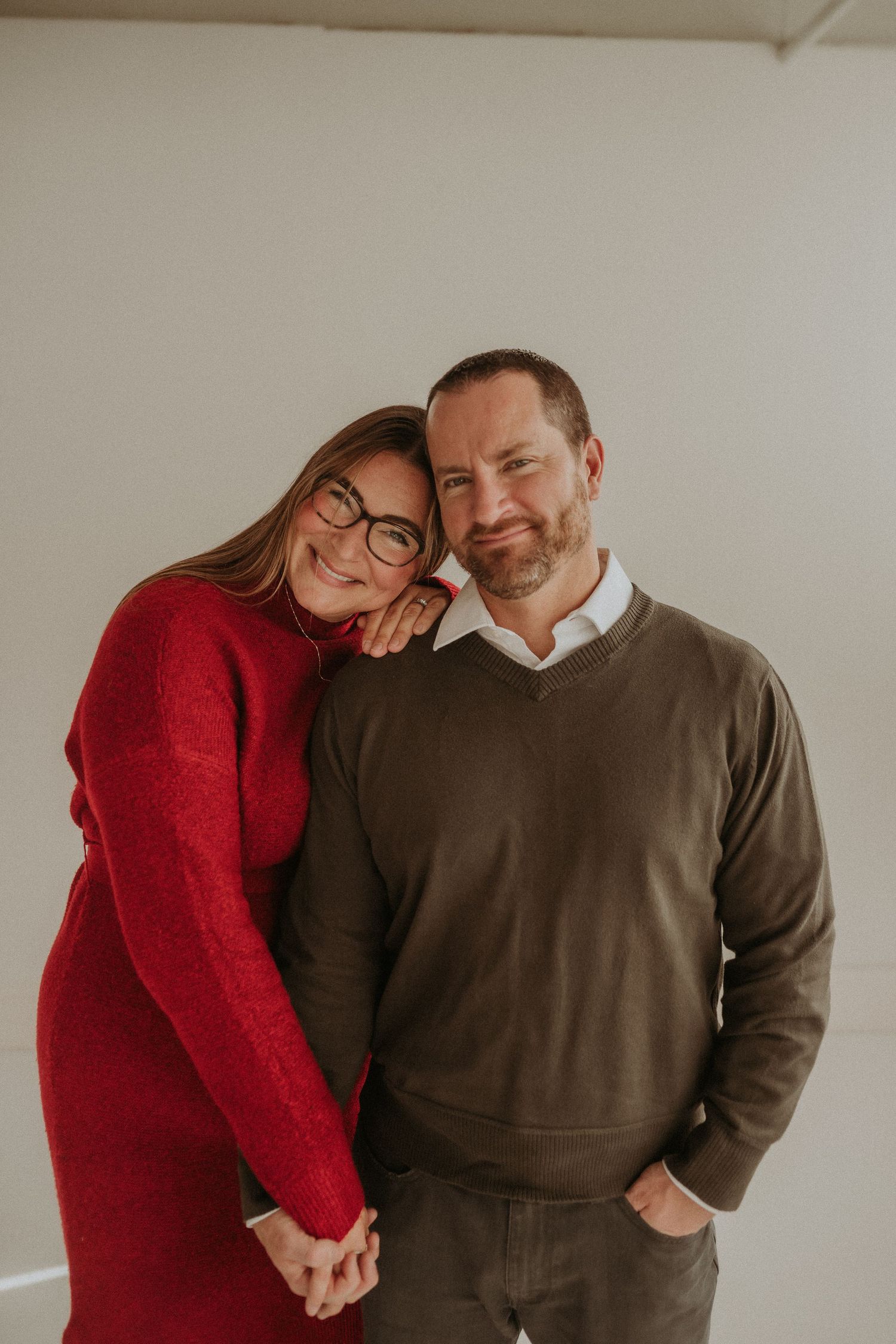 A couple leans in close together while wearing festive winter attire in a bright studio setting.