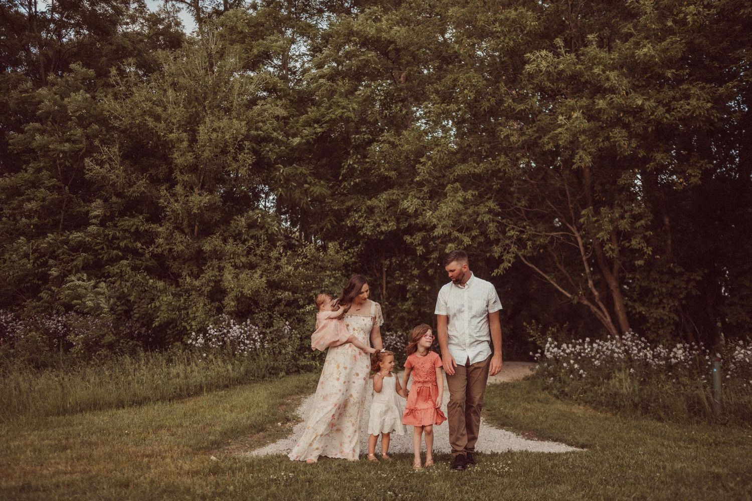 A family strolls together on a gravel path surrounded by lush greenery and trees.