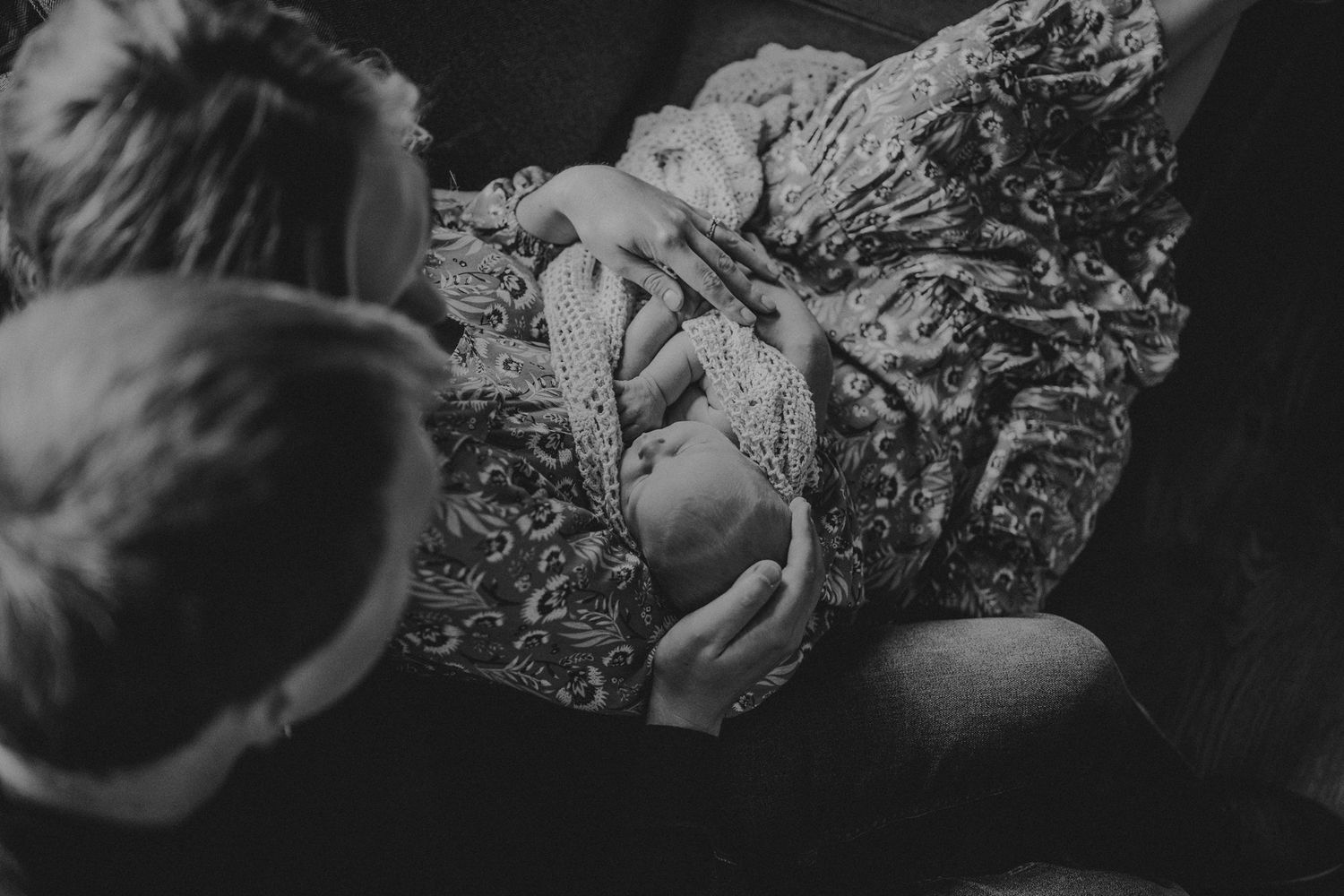 Intimate black and white portrait of newborn being held against textured blanket.
