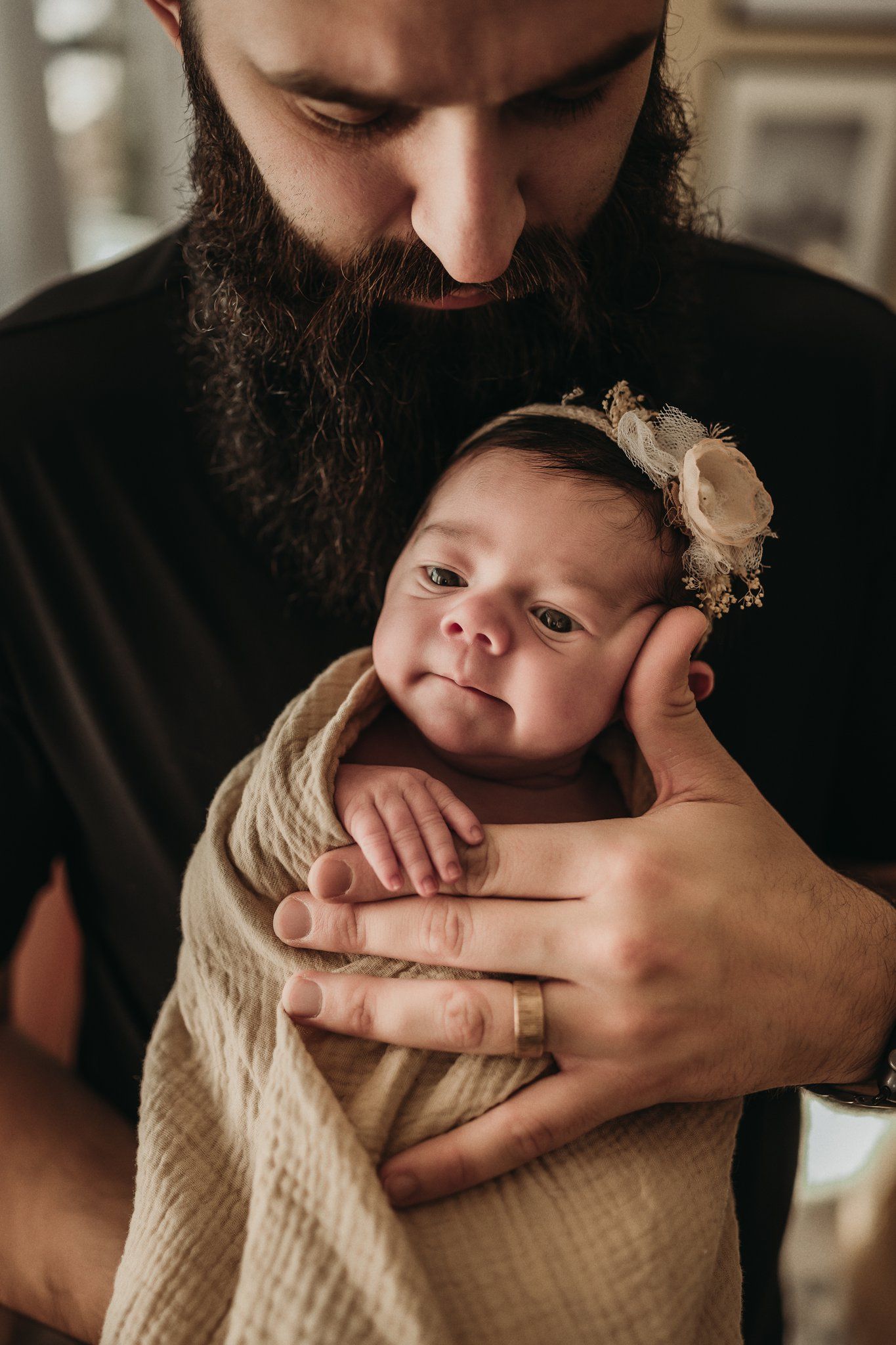 Close up of caring hands holding newborn baby wrapped in cream fabric.