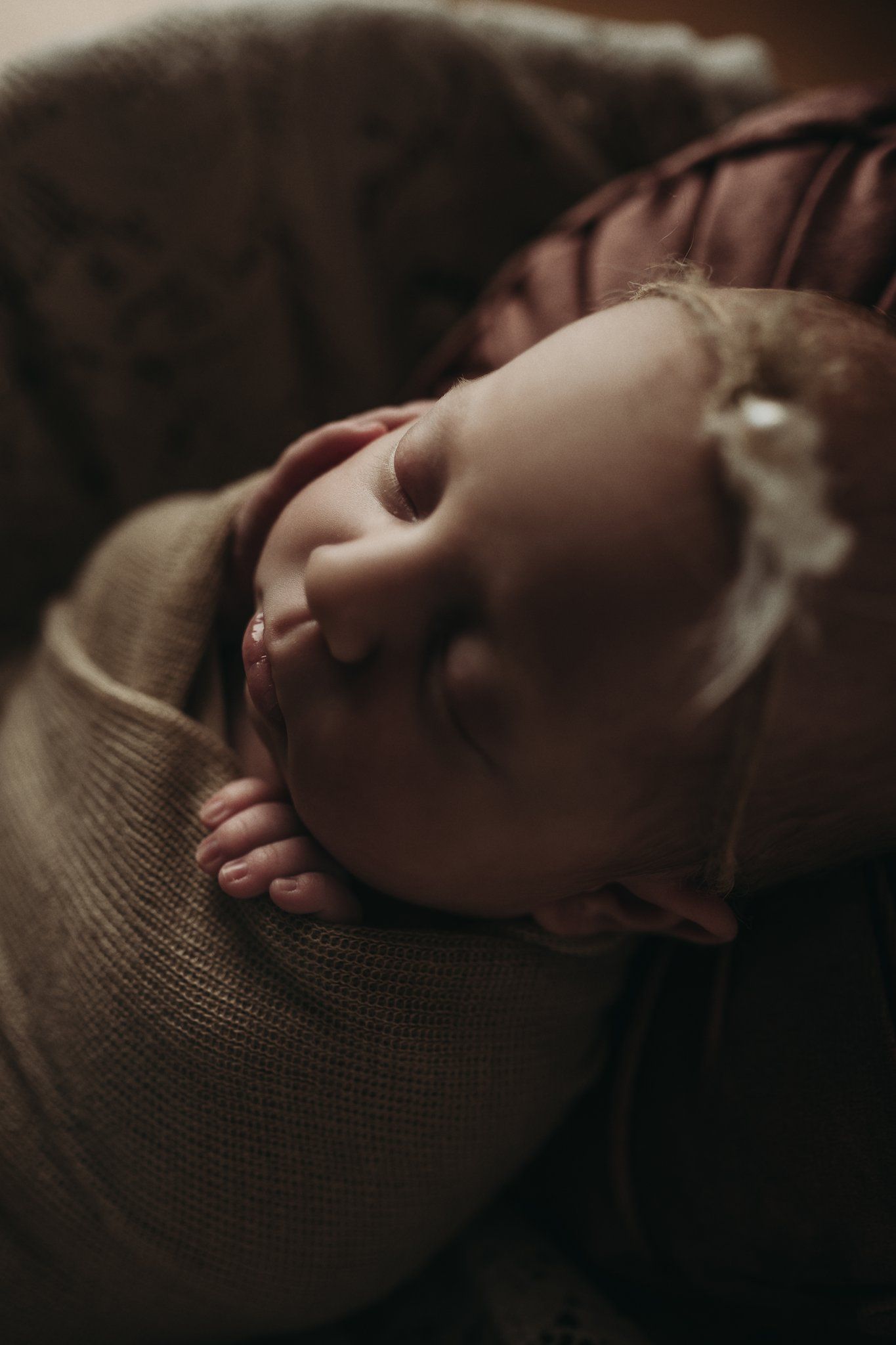 Artistic side profile of sleeping newborn wrapped in textured fabric against dark background.