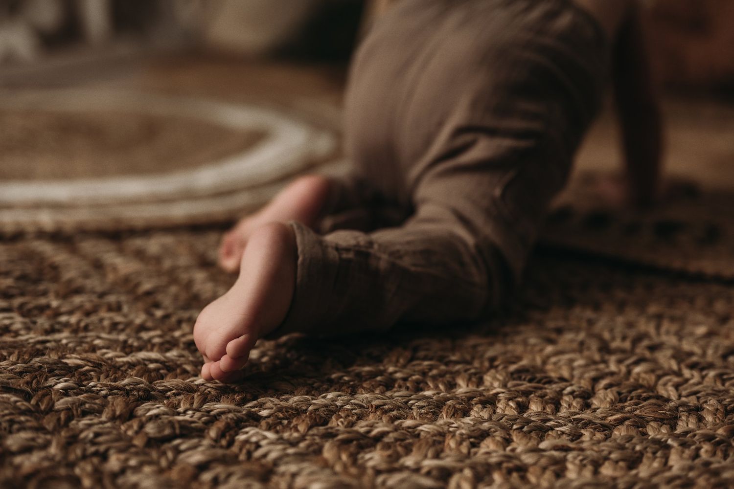 Small bare feet resting on a textured brown carpet in warm moody lighting.